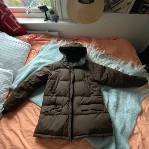 Brun dunjacka från Everest - Säljer en brun dunjacka från Everest i storlek 42. Jackan är perfekt för kalla vinterdagar med sin varma vaddering och långa ärmar. Den har en praktisk huva och stängs med dragkedja. Jackan är i mycket bra skick och redo för nya äventyr!