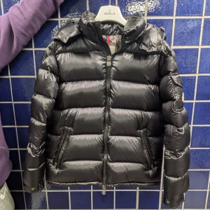 Svart dunjacka från Moncler - Säljer en snygg svart dunjacka från Moncler i mycket bra skick. Jackan har en quiltad design med dragkedja och en praktisk ficka på ärmen. Perfekt för kalla vinterdagar och håller dig varm och stilren. Passar både till vardags och festliga tillfällen. Kvitto tillkommer såklart.