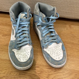 Nike Air Jordans i blått och vitt - Säljer ett par Nike Air Jordans i blått och vitt. Skorna har en cool vintage-look med ljusblå snörning och en hög modell. Perfekta för både vardag och fest! De är i bra skick men har lite slitage på sulan. Passar perfekt för dig som vill ha en stilren och sportig look.