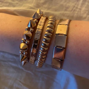Guldarmband i olika stilar - Säljer ett set med fyra guldarmband i olika stilar. Ett armband har spetsiga nitar, ett annat har en slät yta, det tredje har en vriden design och det fjärde har en länkstil. Perfekt för att mixa och matcha till olika outfits!