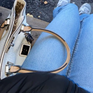 Vit handväska från Guess - Selling a nice white handbag from Guess with beige handle and leopard print lining. The bag has a stylish design with metal buckles and a decorative chain. Perfect for both everyday and parties! Note that the handle has some wear.🩷you can also suggest a price