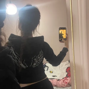 Svart hoodie med glittriga detaljer - Säljer en snygg svart hoodie från Juicy Couture med glittriga vingar på ryggen och text på framsidan. Den har en dragkedja och är supermjuk, perfekt för en chill dag eller en utekväll. Passar perfekt till höst och vinter! GoodGirl size XXS-S