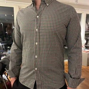 Rutig skjorta från Paul & friends - Snygg rutig skjorta från Paul & friends i storlek M. Skjortan har en klassisk design med knappar och långärmade ärmar. Färgerna är en mix av grönt, brunt och vitt! Nypris 1200kr och hör av dig vid intresse! 