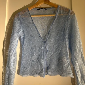 Ljusblå spetskofta - Säljer en elegant ljusblå spetskofta med knappar framtill. Koftan har långa ärmar och en v-ringad design, perfekt för att lägga till en romantisk touch till din outfit. Passar bra till både vardag och speciella tillfällen.