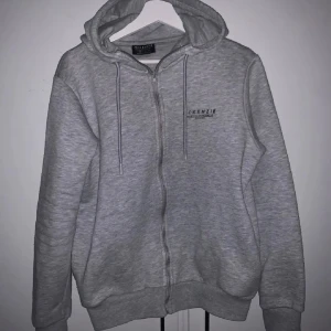 Grå hoodie från McKenzie - Säljer en grå hoodie från McKenzie med dragkedja och huva. Tröjan har långa ärmar och ribbade muddar vid ärmslut och nederkant. Perfekt för en avslappnad stil.