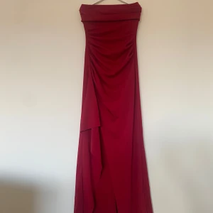 Vinröd axelbandslös långklänning - Elegant vinröd axelbandslös långklänning med draperad design. Perfekt för en festlig kväll eller bal.