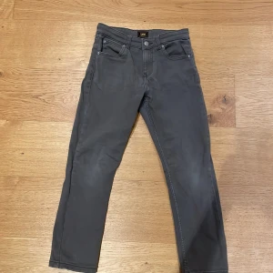 Grå jeansbyxor från Lee - Snygga grå jeansbyxor från Lee med klassisk femficksdesign och knappgylf. Perfekta för en stilren look. Byxorna har en normal passform och är tillverkade i ett slitstarkt material.