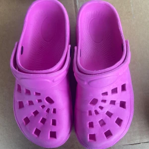 Rosa sandaler med hålmönster - Säljer ett par rosa sandaler i syntetmaterial med ett unikt hålmönster. De har en justerbar rem för bättre passform och är perfekta för sommarens varma dagar.