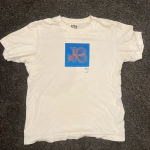 Vit t-shirt med grafiskt tryck från Uniqlo - Säljer en vit t-shirt från Uniqlo med ett coolt grafiskt tryck i blått och grönt. T-shirten har en normal passform och är kortärmad, perfekt för en avslappnad stil.