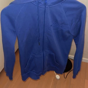 Lila kofta från Peak Performance - Säljer en snygg blå hoodie från Peak Performance. Den har en dragkedja framtill och en broderad logga på bröstet