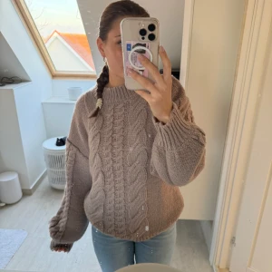 Beige stickad tröja från Sofie Schnoor - Mysig beige stickad tröja från Sofie Schnoor med flätmönster framtill. Tröjan har en hög krage och långa ärmar, perfekt för kyliga dagar. 