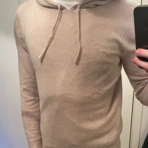 Beige cashmere hoodie  - Säljer en supermjuk beige hoodie i cashmere.  Den har en justerbar huva med dragsko och långa ärmar. Ett måste för garderoben! Defekt i armen på bild 3 men syns knappt. 