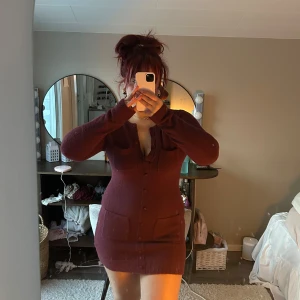 Vinröd stickad klänning - Aldrig använd! Säljer en snygg vinröd stickad klänning med knappar framtill och två praktiska fickor. Klänningen har en tight passform och långa ärmar, perfekt för kyligare dagar. Den är både stilren och bekväm, vilket gör den till ett mångsidigt tillskott i garderoben.