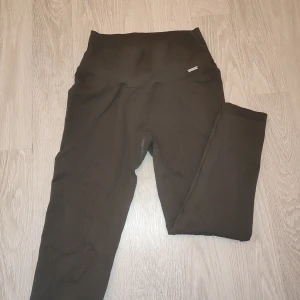 Gröna ribbade leggings från Aim'n - Snygga ribbade leggings från Aim'n med hög midja i färgen khaki. Perfekta för både träning och avslappning. De har en tight passform som framhäver figuren och ger bra stöd. De är lite slitna i en av sömmarna men annars är den i väldigt bra skick.