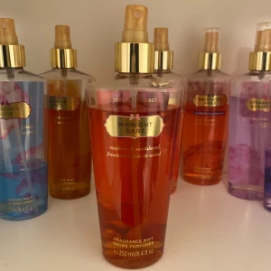 Midnight Dare Fragrance Mist från Victoria's Secret - En doftspray från Victoria's Secret med namnet Midnight Dare. Flaskan är röd och har en guldig spraypump. Doften innehåller toner av hallon och sandelträ. Perfekt för att fräscha upp din dag med en söt och träig doft.