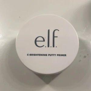 C-Brightening Putty Primer från e.l.f. - En C-Brightening Putty Primer från e.l.f. i en rund, vit burk. Denna primer är designad för att ge en ljusare och jämnare hudton, perfekt som bas för smink.