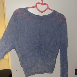 Lavendelfärgad spetsblus - Säljer en elegant lavendelfärgad spetsblus med långa ärmar. Blusen har en vacker spetsdesign och en knutdetalj framtill som ger en unik touch. Perfekt för att lägga till en romantisk känsla till din outfit. Vida armar 