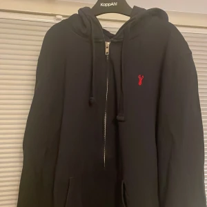 Mörkblå hoodie från Next - Säljer en stilren mörkblå hoodie från Next i storlek S. Den har en dragkedja framtill och en liten röd broderad detalj på bröstet. Tillverkad i 100% bomull, perfekt för en avslappnad stil.