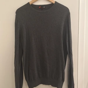 Grå tröja från Dressmann - Säljer en stilren grå tröja från Dressmann i mjuk pima bomull. Tröjan har en klassisk rund hals och långa ärmar, perfekt för en avslappnad look. Passar bra till både jeans och chinos, 9,5/10 i skick, Pris kan diskuteras 