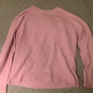 Rosa stickad tröja - Mysig rosa stickad tröja med långa ärmar och ribbade kanter. Perfekt för kyliga dagar och ger en skön och avslappnad stil. Passar bra till jeans eller kjol för en casual look.