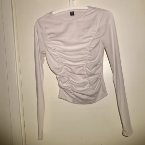 Vit långärmad topp från Shein  - Säljer en stilren vit långärmad topp från Shein Bae. Snygg rynkad detalj framtill som med en tightare passform runt mage o midja. Perfekt för att lyfta din outfit, använd fåtal gånger 