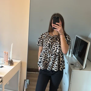 Leopardmönstrad blus med volang - Trendig leopardmönstrad blus med volangdetaljer och korta ärmar. Perfekt för att ge en stilfull touch till din outfit. Blusen har en lös passform och knytning framtill.