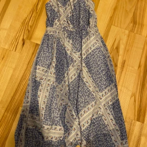 Blåmönstrad klänning från H&M - Charmig blåmönstrad klänning från H&M med smala axelband och ett vackert blommigt mönster. Klänningen har en luftig passform och är perfekt för varma dagar. Den har en vit underkjol som ger extra komfort och stil. Perfekt till finare tillfällen som kalas, examen, bröllop osv.