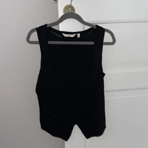 Svart väst från Riley - Snygg svart väst från Riley i storlek S. Västen har en klassisk design med knappar framtill och en stilren look. Perfekt för att lägga till en extra touch till din outfit.😗