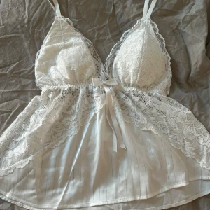 Vit spetslinne med rosett - Sött vitt linne med spetsdetaljer och en söt rosett framtill. Nyskick, storlek L men är liten i storlek så passar även som  XS/S