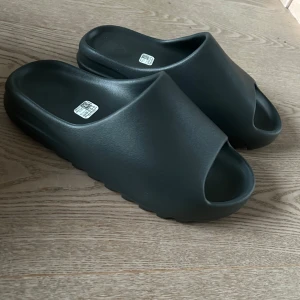  Yeezy slides, dark onyx - Säljer mina helt nya YZY Slides i färgen dark onyx från Adidas i storleken 44. Perfekta för sommaren med en bekväm passform och ribbad sula för extra grepp. Enkla att matcha med olika outfits. Kontakta mig vid minsta fundering 🙌