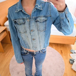 Blå croppad jeansjacka från FB Sister - Blå croppad jeansjacka från FB Sister. Jackan har en klassisk krage, knappar framtill och två bröstfickor med lock. Den har en rå kant nertill. Original Jeans så väldigt slitstarkt och hårt material. Jag är 163 cm. 💙