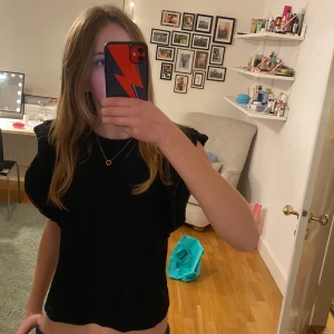 Svart topp med volangdetaljer - Säljer en svart topp med volangdetaljer på ärmarna. Den är i bra skick och passar perfekt för både vardag och fest. Toppen är i ett mjukt material och har en normal passform. Perfekt för att styla med jeans eller kjol!