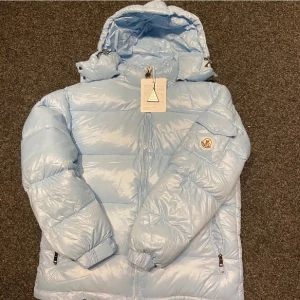 Ljusblå dunjacka - Säljer en superfin ljusblå dunjacka . Den är perfekt för kalla dagar med sin fluffiga och varma design. Jackan har en dragkedja framtill och en mysig huva. Den är i mycket bra skick och redo för vinterns äventyr! ❄️