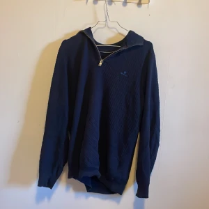 Mörkblå Gant halvzip  - Säljer en mörkblå tröja med dragkedja i kragen. Den har en diskret struktur och långa ärmar. Perfekt för kyliga dagar och passar bra till både vardag och lite finare tillfällen.