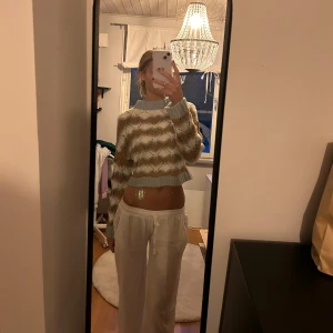 Mönstrad stickad tröja - Säljer en superfin stickad tröja med ett unikt mönster i beige, vit och ljusblå. Den är croppad och har långa ärmar, perfekt för både höst och vår. Tröjan är i bra skick och passar perfekt för en avslappnad stil. Perfekt att matcha med jeans eller kjol!