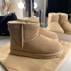 Supermysiga beige boots från UGG i mocka med fluffigt foder. Perfekta för kalla dagar när du vill hålla fötterna varma och bekväma. De har en klassisk design med rund tå och en robust sula för bra grepp. Passar perfekt till både vardag och avslappnade tillfällen. Äkta, helt nya aldrig använt, Tyvär var det ej min storlek! Lite ljusare än vad dem är på bild.❤️