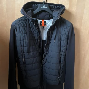 Svart hybridjacka från Parajumpers - Säljer en snygg svart jacka från Parajumpers i mycket bra skick. Jackan har en quiltad design med dragkedja och huva. Perfekt för höst och vår, med långa ärmar och en stilren look. Passar både till vardags och lite finare tillfällen. Storlek L