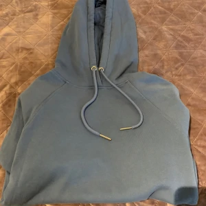 Mörkblå hoodie - Säljer en snygg och bekväm mörkblå hoodie i bra skick. Den har en klassisk design med justerbar huva och ribbade muddar vid ärmslut och nederkant. Perfekt för både vardag och mysiga stunder hemma. Passar till det mesta i garderoben!