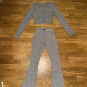 Grå ribbad kofta och byxor från Fashion Nova - Säljer en superfin grå ribbad kofta från Fashion Nova. Den är croppad med knappar framtill och har långa ärmar. Perfekt för en chill dag eller att styla upp för en utekväll. Passar bra till både jeans och kjol! och dessutom breda byxor till outfiten. 