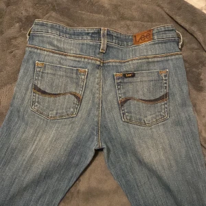 Blå jeans från Lee - Säljer ett par snygga blå jeans från Lee i modellen Rice Flare. De har en klassisk femficksdesign och är i bra skick. Perfekta för både vardag och fest! 