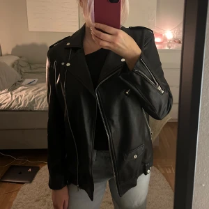 Svart skinnjacka från Stradivarius - Säljer en snygg svart skinnjacka från Stradivarius i storlek S. Lite oversized i modellen vilket gör att den passar fler storlekar beroende på hur man vill att den ska sitta. Använd endast 1 gång