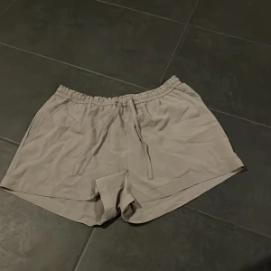 Beige shorts från Rangelology - Säljer ett par snygga beige shorts från Rangelology i storlek M. De har en elastisk midja för extra komfort och två praktiska fickor. Perfekta för en avslappnad sommarstil eller träning. Materialet känns lätt och luftigt, vilket gör dem idealiska för varma dagar.