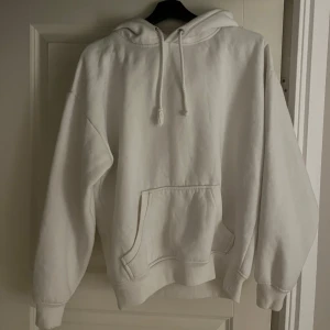 Vit hoodie från Bik Bok - Mysig vit hoodie från Bik Bok i storlek XS. Perfekt för kyliga dagar med sin mjuka insida och praktiska ficka framtill. Den har en klassisk design med dragsko i huvan och ribbade muddar vid ärmslut och nederkant. Passar till alla tillfällen!