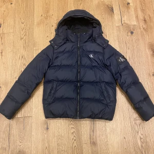 CK Jacka - Riktig snygg Jacka från Calvin Klein endast använd ca en halv vinter i otroligt bra skick inga skador. Den har även en praktisk innerficka och man kan ta av luvan med en dragkedja. Den passar både tjejer och killar. Ny pris ca 2500kr Kan tänka mig att gå ner i pris.   Köparen står för frakt!!🚚