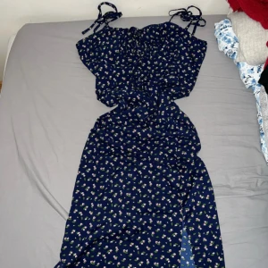 Blommig klänning med knytband - Söt blommig klänning i mörkblått med små vita och rosa blommor. Den har knytband vid axlarna och en fin slits framtill. Perfekt för sommarens fester eller en mysig dag i parken. Klänningen är i bra skick och redo för nya äventyr! Det är storlek S och är ifrån Shein