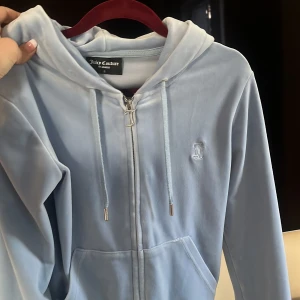 Ljusblå hoodie & byxor  från Juicy Couture - Säljer en supermjuk och snygg ljusblå hoodie från Juicy Couture. Den har dragkedja fram och en klassisk luva med snören. Perfekt för en chill dag eller när du vill vara bekväm men ändå se stilren ut. Den har också praktiska fickor framtill. Byxor stl xxs och Hoodie S