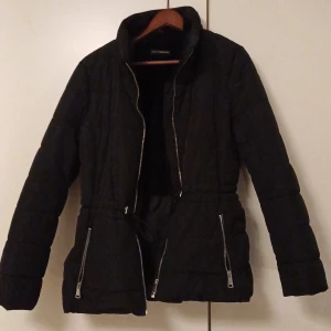 Svart quiltad jacka från KappAhl - Säljer en svart quiltad jacka från KappAhl i bra skick. Den har en dragkedja framtill och praktiska fickor med dragkedjor. Perfekt för höst och vår, med en normal passform och långa ärmar. En stilren och funktionell jacka för vardagsbruk.