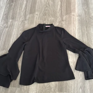 Svart blus med volangärmar - Snygg svart blus med långa volangärmar som ger en elegant touch. Perfekt för både vardag och fest. Materialet känns mjukt och bekvämt mot huden. Passar bra till både jeans och kjol för en chic look. 🖤