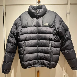 Svart pufferjacka från The North Face - Säljer en svart pufferjacka från The North Face i mycket bra skick. Jackan är perfekt för kalla dagar med sin tjocka vaddering och dragkedja framtill. Den har en klassisk design med långärmade ärmar och är superbekväm. Passar perfekt för både höst och vinter! Liten defekt på jackans front men inget som stör😁 skriv för mer bilder eller frågor!