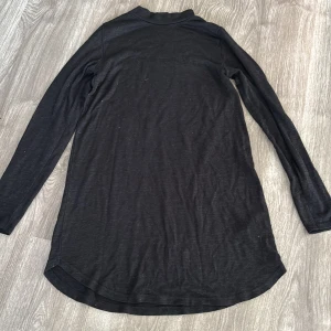 Svart långärmad klänning - Säljer en stilren svart långärmad klänning i mjukt material. Perfekt för både vardag och festliga tillfällen. Tröjan har en enkel design med rundad nederkant som ger en snygg passform. 